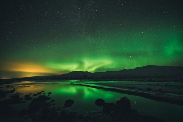 Une magnifique aurore boréale verte se reflétant dans l'eau d'un lac calme sous un ciel nocturne étoilé.