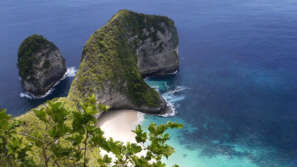 Vue aérienne de Kelingking Beach, une plage isolée sur l'île de Nusa Penida, entourée de falaises verdoyantes et d'eaux turquoise.