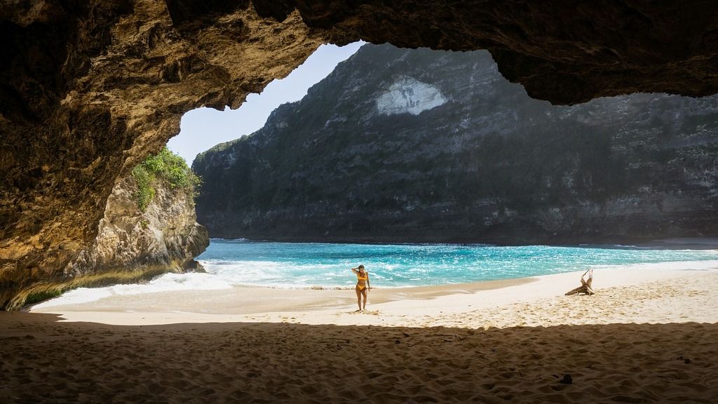 Crique cachée avec une plage de sable doré à Nusa Penida, vue depuis une grotte avec des falaises majestueuses en arrière-plan.
