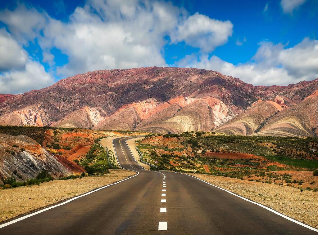 Route pittoresque en Argentine: une route sinueuse menant vers des montagnes colorées sous un ciel bleu.