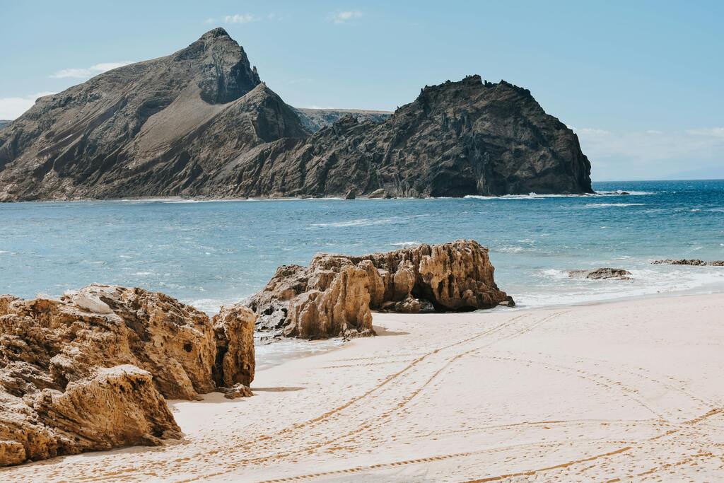 Plage de sable doré avec montagnes rocheuses en arrière-plan.
