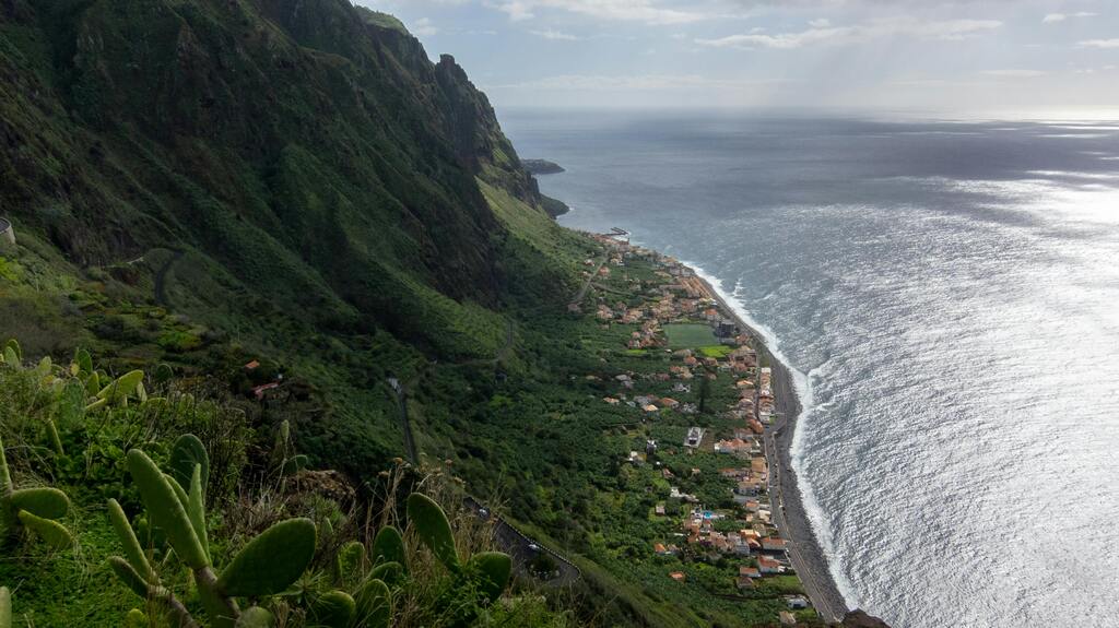 Vue panoramique sur un village côtier entouré de montagnes verdoyantes.
