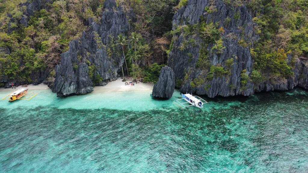 Plage paradisiaque avec eaux cristallines et falaises rocheuses aux Philippines.
