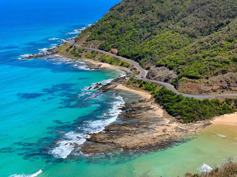 Une vue aérienne de la Great Ocean Road serpentant le long de falaises verdoyantes et de plages aux eaux turquoise en Australie.
