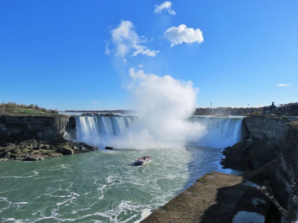 Bateau touristique approchant les chutes du Niagara avec un nuage de brume sous un ciel bleu clair.
