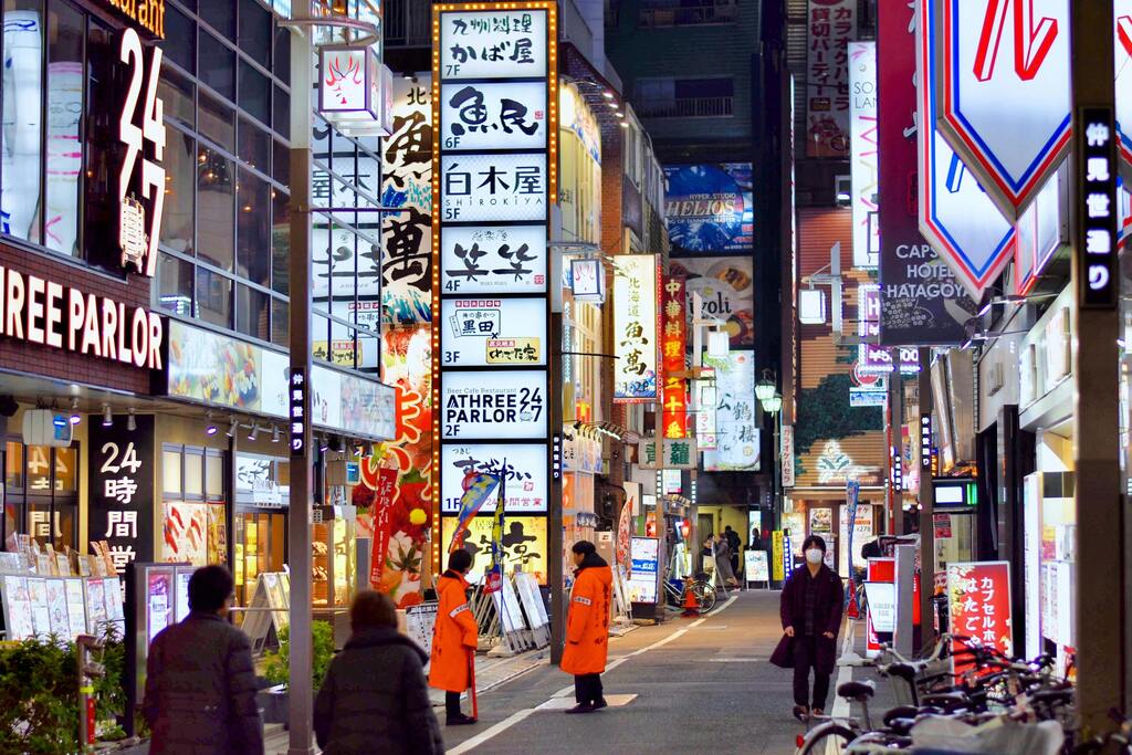 cène animée d'une rue de Tokyo la nuit, illuminée par des enseignes colorées.
