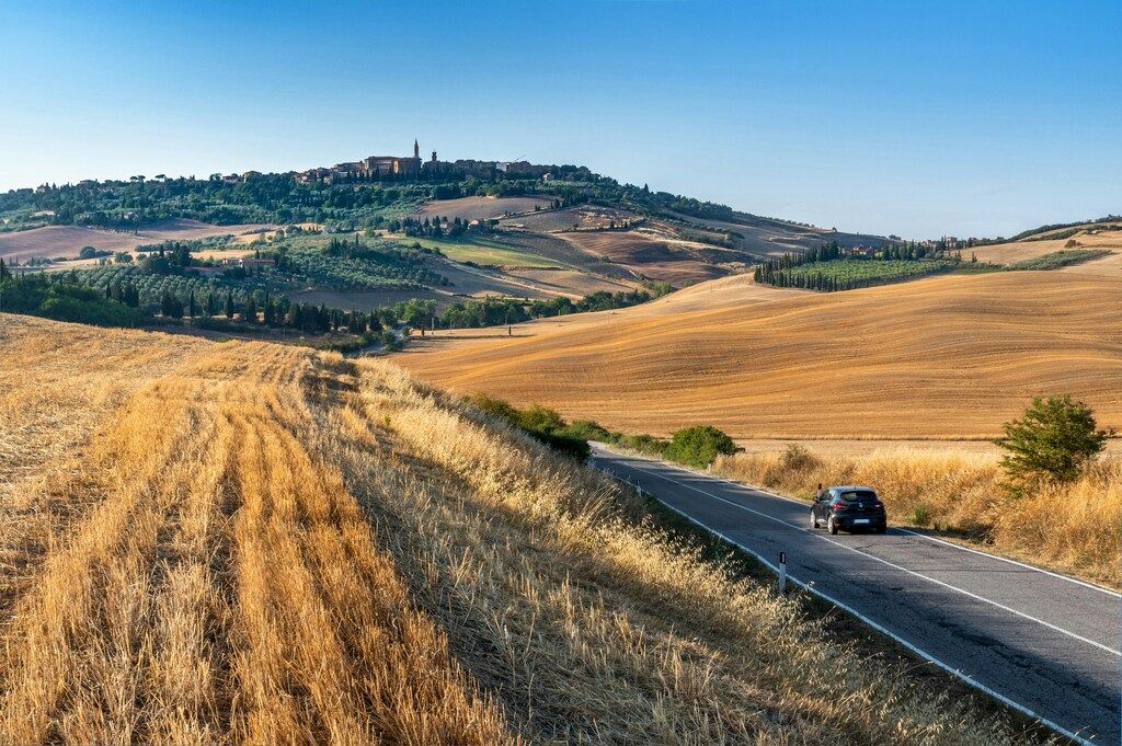 Campagne toscane avec route sinueuse et village médiéval sur la colline