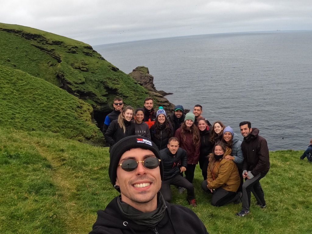 Selfie de groupe WeRoad avec des falaises verdoyantes et l’océan aux îles Féroé en arrière-plan