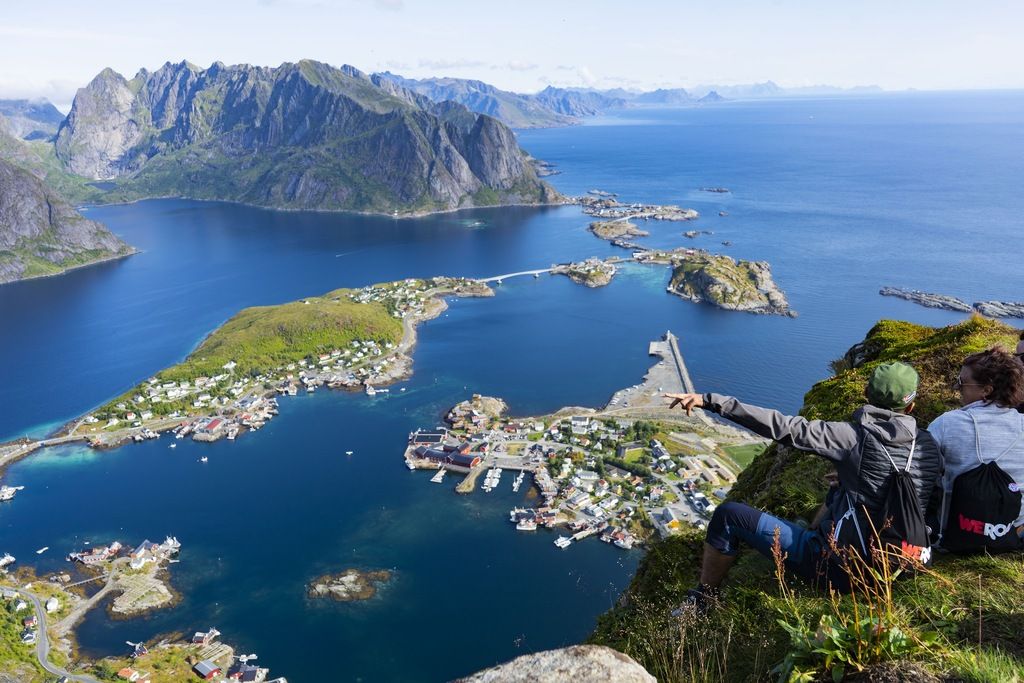 Vue panoramique sur les îles Lofoten avec deux voyageurs assis au sommet d’une falaise