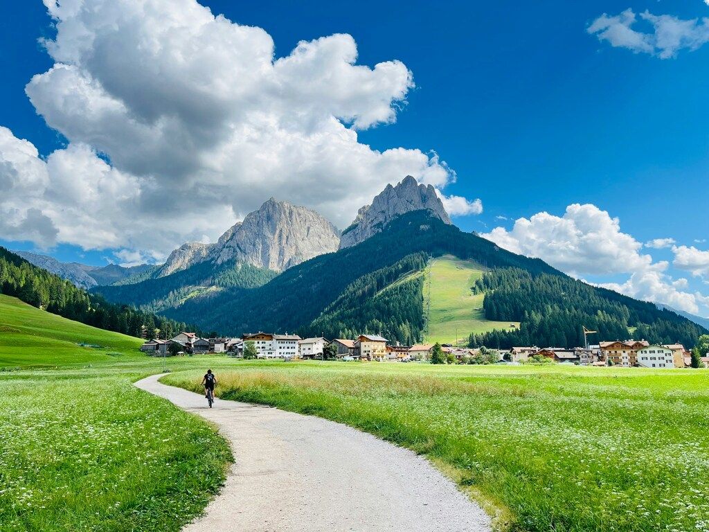 Cycliste pédalant sur un chemin alpin avec vue sur les Dolomites et un village pittoresque au loin