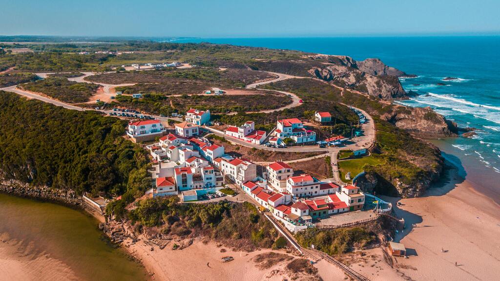 Vue aérienne d’un village côtier pittoresque au sommet d’une falaise au Portugal, entouré par la mer et la plage.