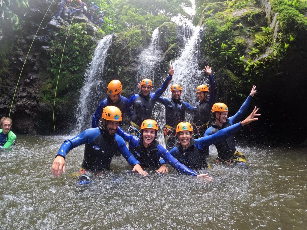 Groupe de voyageurs WeRoad en tenue de canyoning sous une cascade dans la nature sauvage des Açores