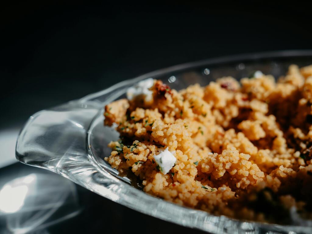 Gros plan d'un plat de couscous à la sicilienne avec morceaux de fromage et herbes aromatiques dans un bol en verre.