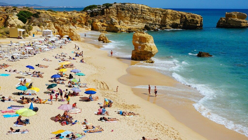 Touristes profitant du soleil sur une plage de sable doré entourée de formations rocheuses en Algarve.