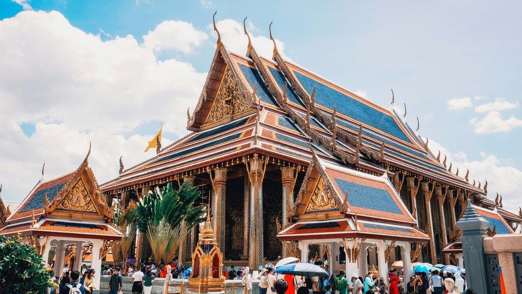 Façade dorée et toits bleus du Grand Palais de Bangkok, avec des visiteurs.