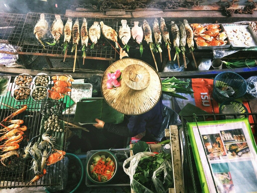 Vue plongeante d'un stand de marché thaïlandais vendant du poisson grillé, des fruits de mer et des légumes frais.