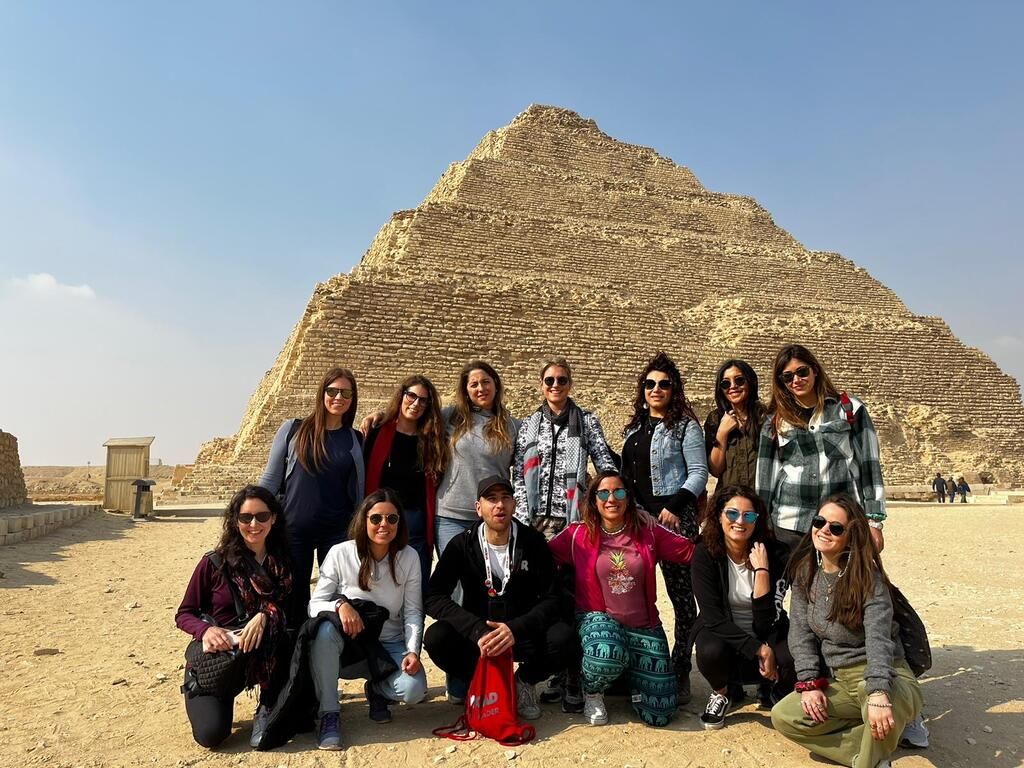 Un groupe de voyageurs WeRoad pose devant la pyramide à degrés de Saqqarah, dans le désert égyptien.