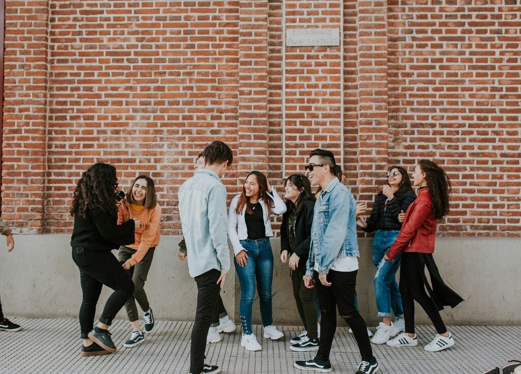 Groupe de jeunes qui rient et discutent ensemble devant un mur en briques rouges.