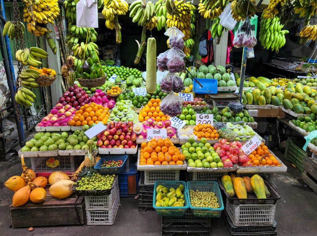 Étal coloré de fruits tropicaux dans un marché local, avec mangues, papayes, bananes, oranges, goyaves et pastèques.