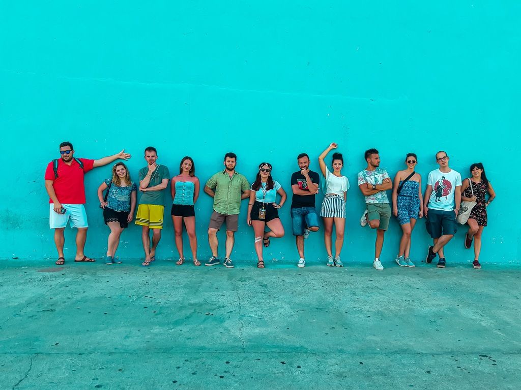 Groupe de voyageurs WeRoad posant de manière décontractée devant un mur turquoise vif, dans une ambiance estivale.