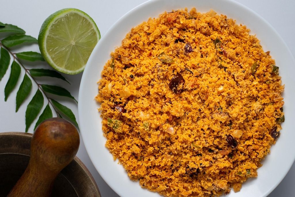 Bol de pol sambol, un mélange traditionnel sri lankais de noix de coco râpée, épices et piments, accompagné d’un demi-citron vert et de feuilles de curry.