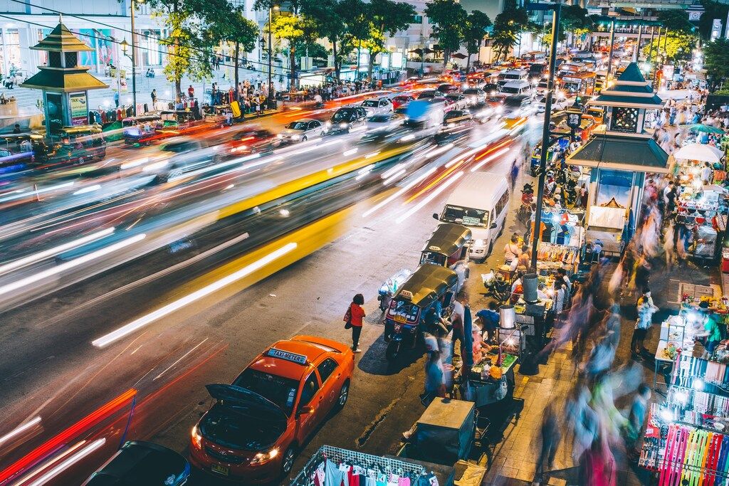 Vue de nuit d'une rue animée de Bangkok avec le mouvement des véhicules et un marché de rue.
