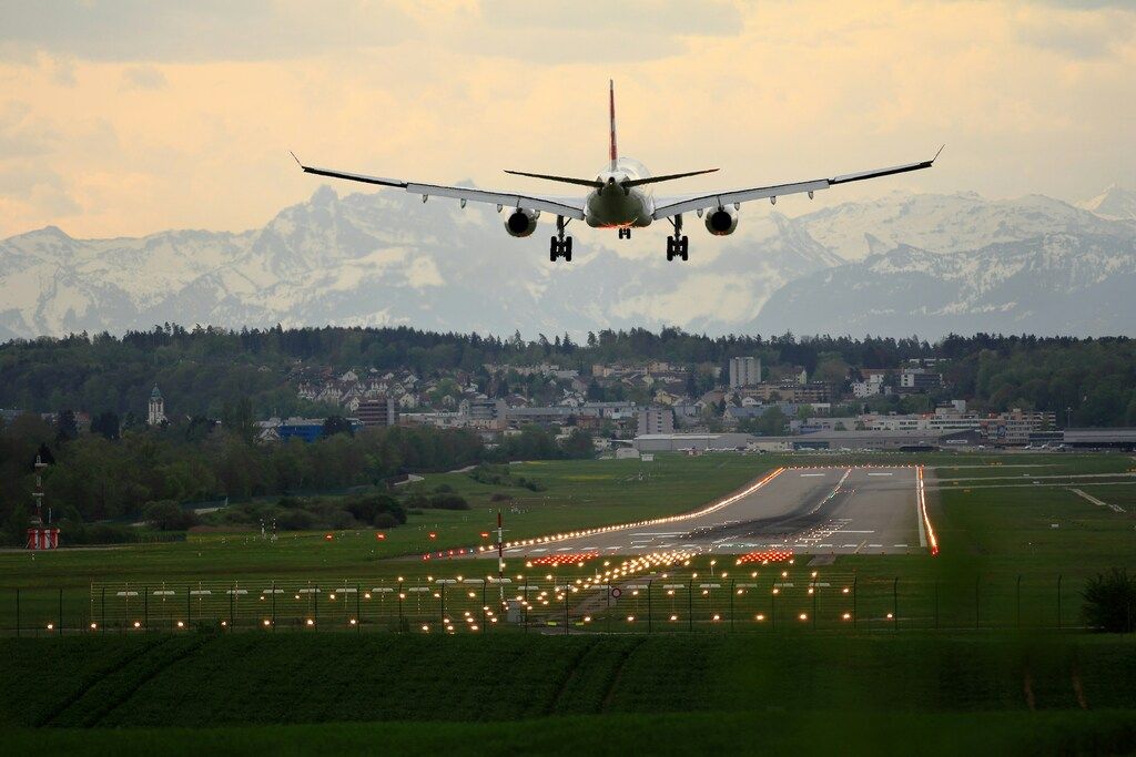 Avion de ligne atterrissant sur une piste entourée de verdure, avec en arrière-plan les Alpes enneigées.