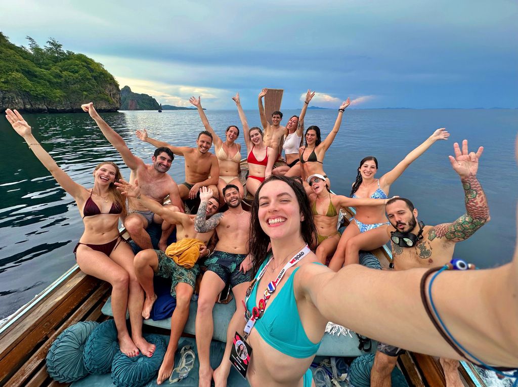 Voyageurs WeRoad profitant d’une excursion en bateau dans une baie tropicale, sourires et maillots de bain sous le ciel bleu