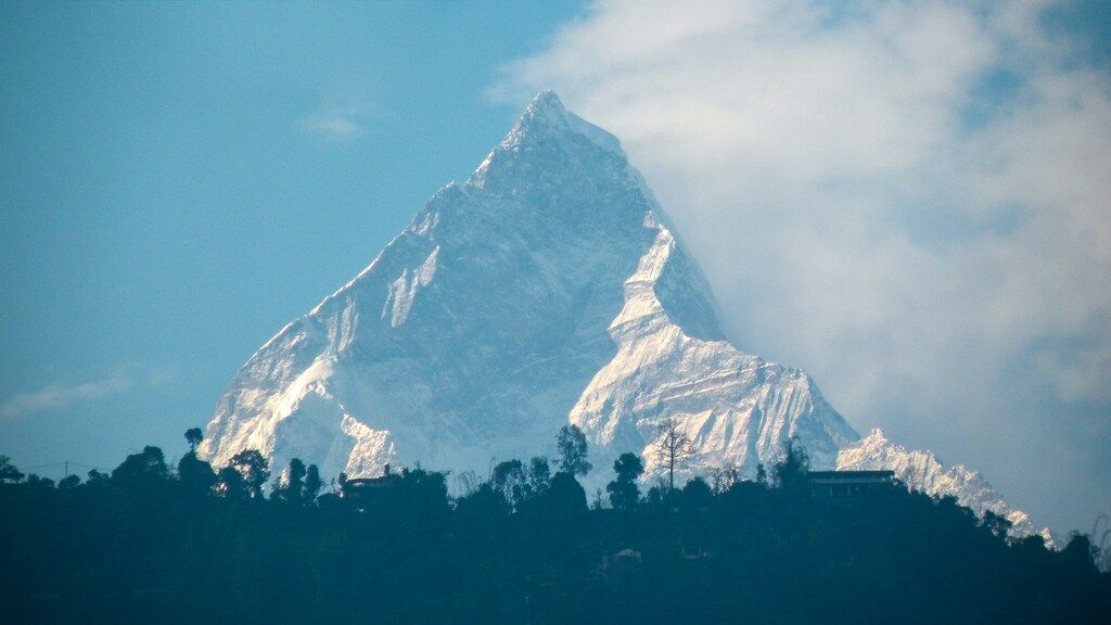 Le Machapuchare, sommet iconique en forme de flèche, sous un ciel bleu avec quelques nuages.
