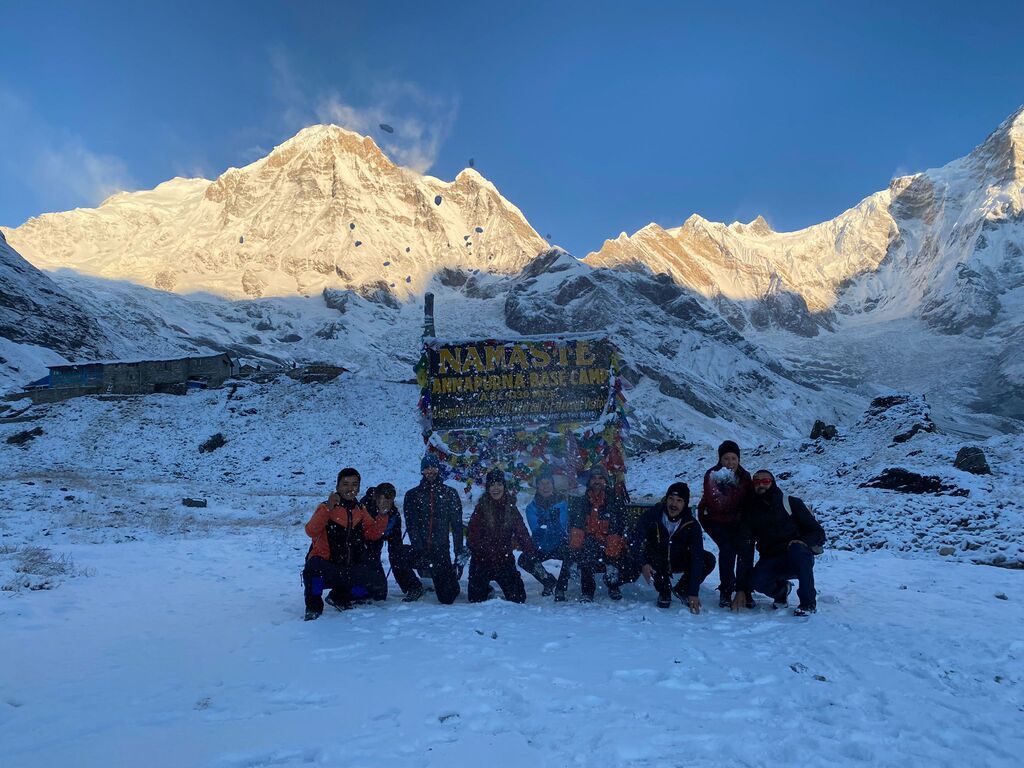 Groupe de trekkeurs posant au camp de base de l’Annapurna, entouré de neige et de montagnes.