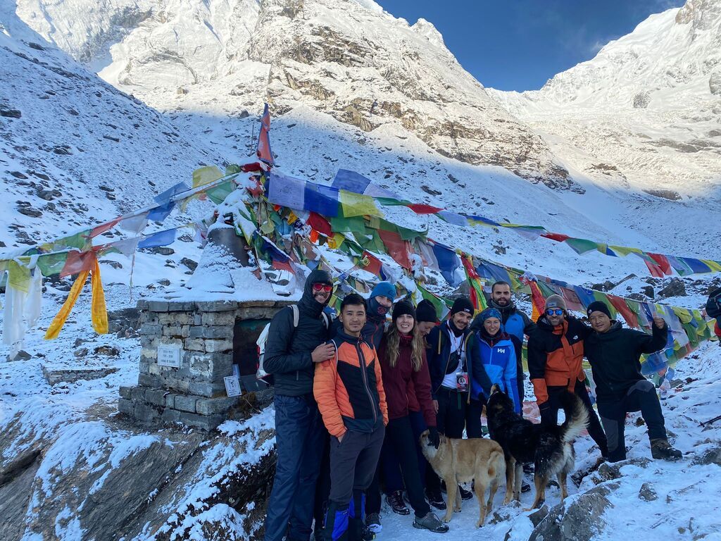 Groupe WeRoad souriant dans la neige himalayenne, drapeaux de prière tibétains en arrière-plan.