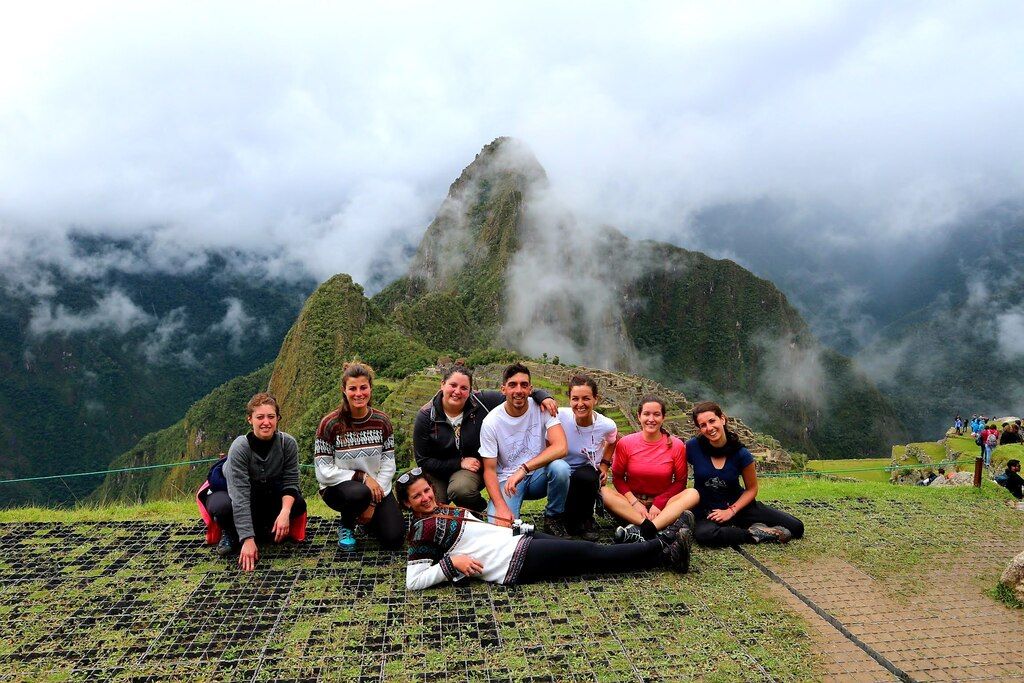 Groupe de jeunes voyageurs posant ensemble devant les montagnes embrumées du Machu Picchu lors d’un voyage de groupe WeRoad de dernière minute.