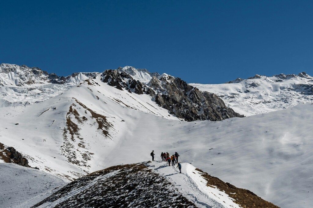Marcheurs en file indienne sur une crête enneigée avec vue panoramique sur les sommets himalayens.