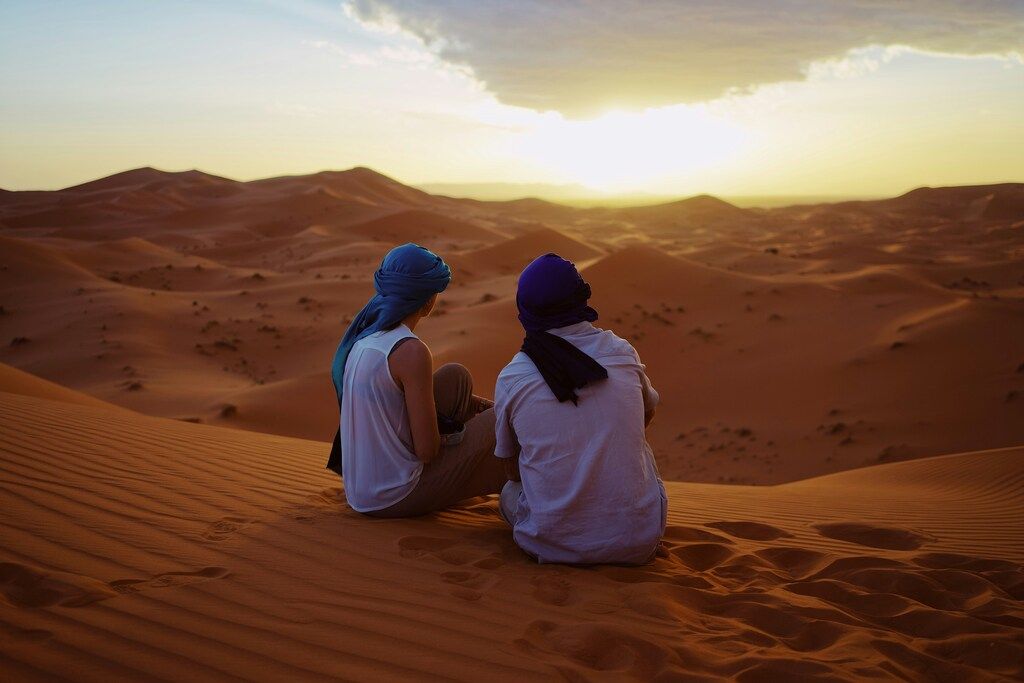 Deux voyageurs assis sur une dune observant le coucher du soleil dans le désert
