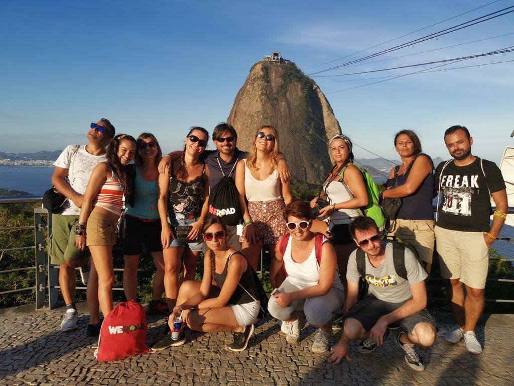 Un groupe de voyageurs WeRoad posant ensemble sur une terrasse panoramique avec le mont Pain de Sucre en arrière-plan à Rio de Janeiro.