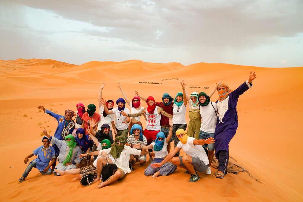 Groupe WeRoad célébrant dans les dunes du Sahara en tenues colorées