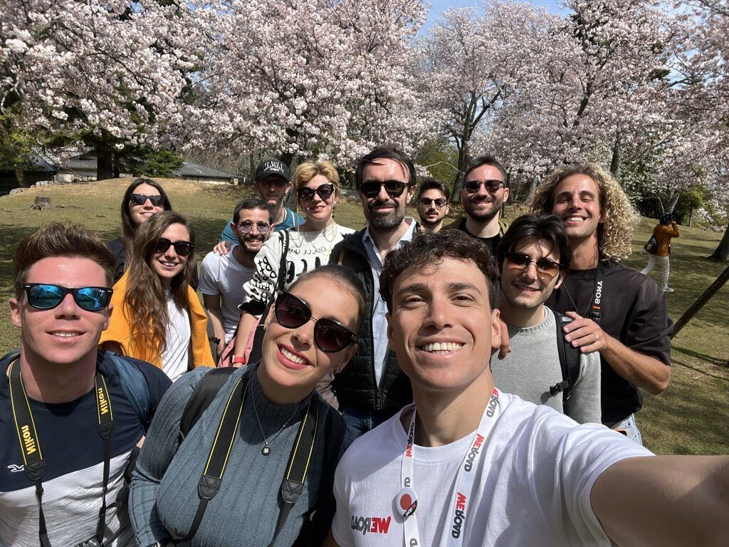 Selfie de un groupe WeRoad souriant sous des cerisiers en fleurs (sakura) au Japon.