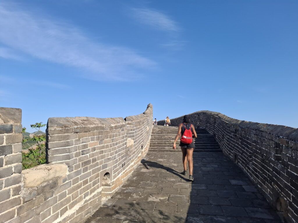 Voyageuse WeRoad marchant sur la Grande Muraille de Chine sous un ciel bleu dégagé.