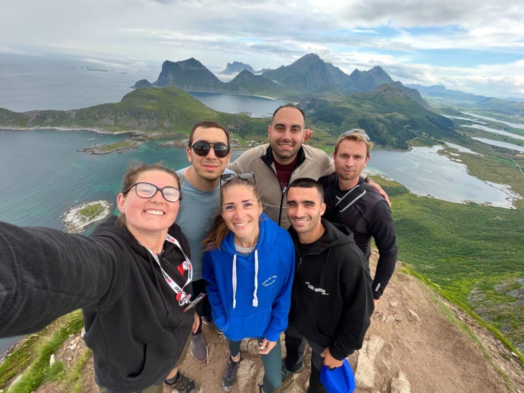 Un groupe de voyageurs Weroad sourit sur un sommet de montagne en Norvège, avec une vue panoramique sur les fjords et les lacs.