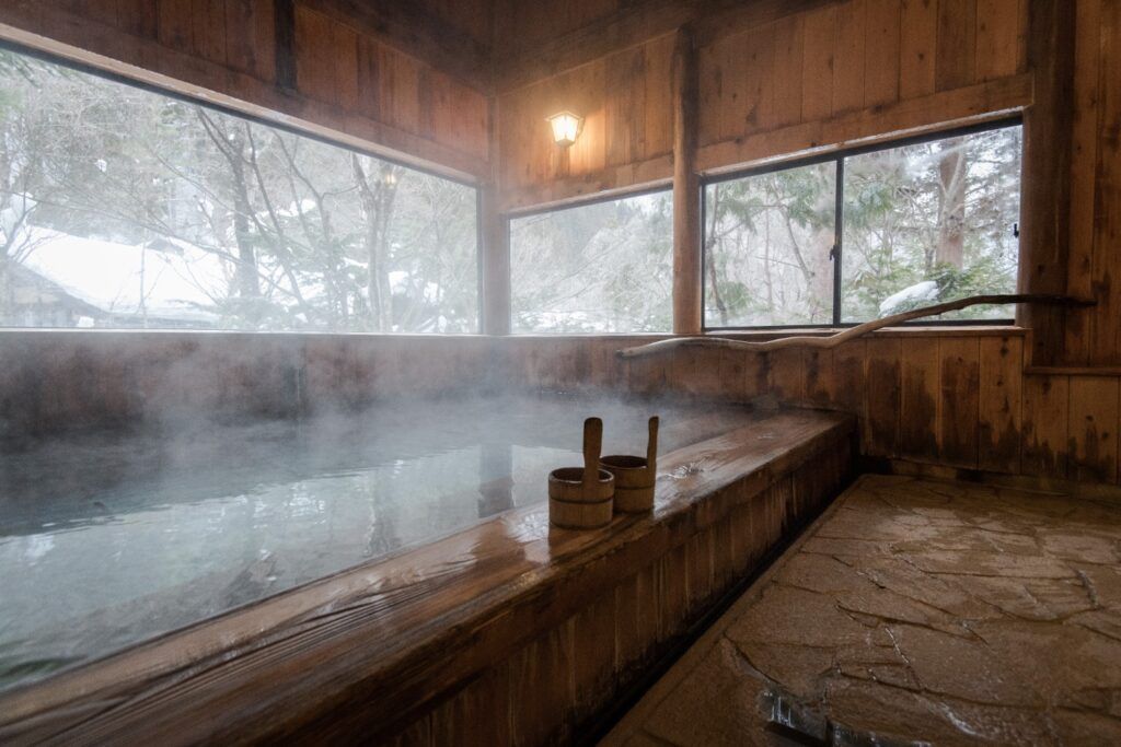Bain chaud (onsen) intérieur en bois embué, avec une vue sur un paysage extérieur enneigé.