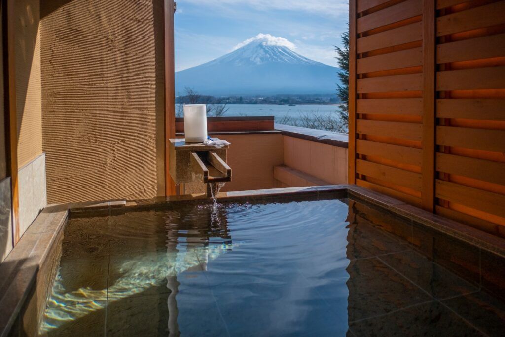 Bain japonais (onsen ou ofuro) extérieur en bois avec une vue spectaculaire sur le Mont Fuji enneigé.