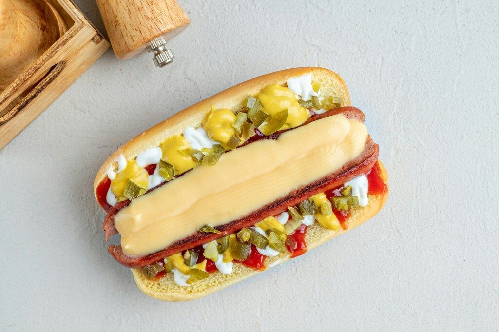 Gros plan sur un Pylsur, le hot-dog emblématique islandais, garni de fromage fondu et de condiments.