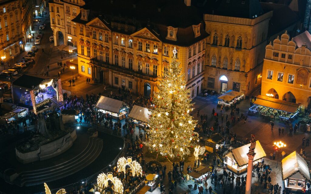 Vue aérienne du Marché de Noël de Prague la nuit, avec le sapin illuminé au centre.