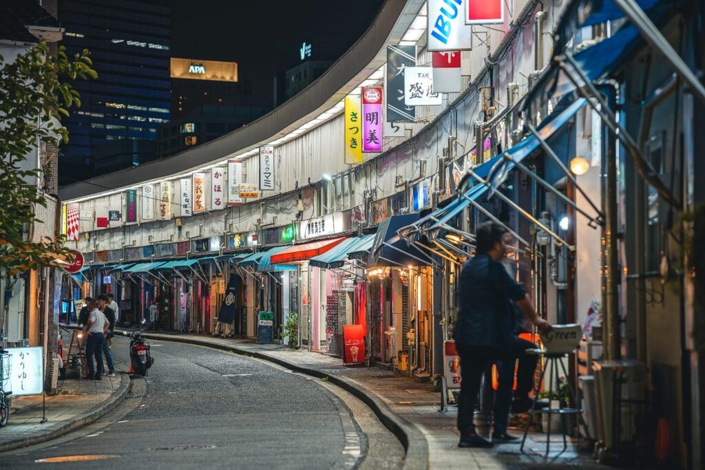 Allée nocturne du Harmonica Yokocho à Kichijoji, bordée de petits stands, néons et devantures cintrées typiques.