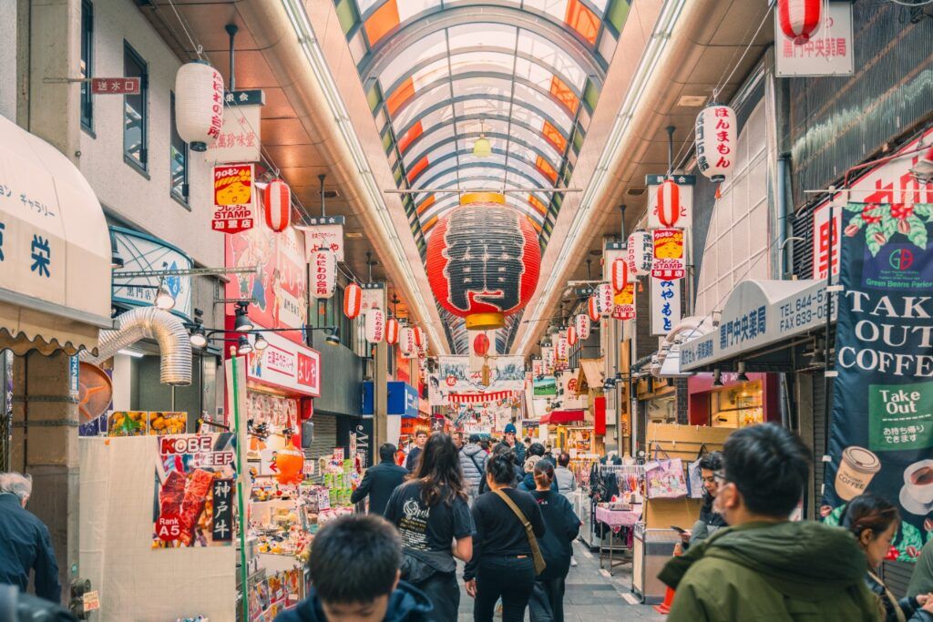 Allée centrale très animée du marché de Kuromon (Osaka), avec des enseignes, des stands de nourriture et de grandes lanternes rouges traditionnelles.