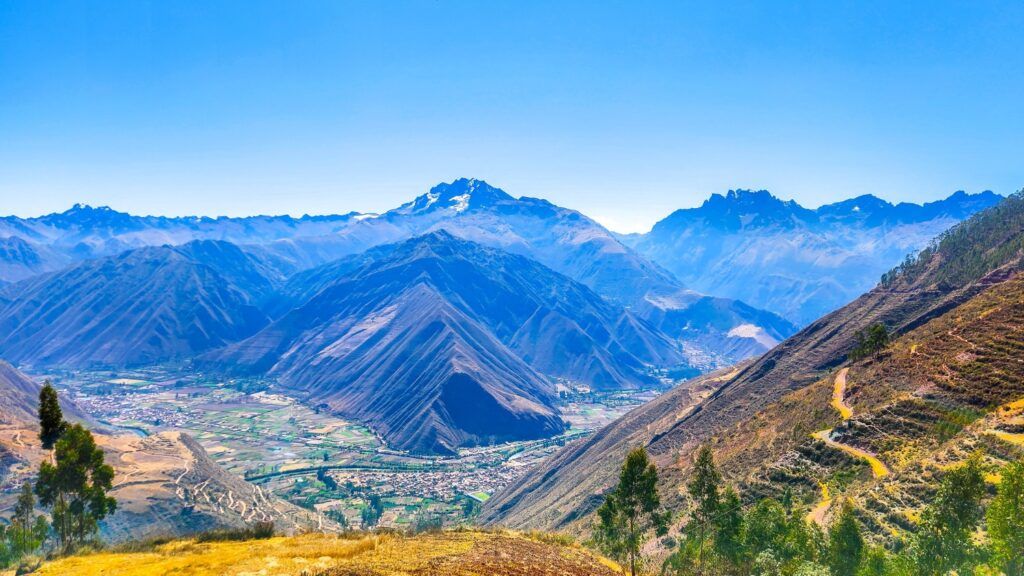 Magnifique panorama de la Vallée Sacrée des Incas baignée de soleil, avec des montagnes andines imposantes aux crêtes acérées.
