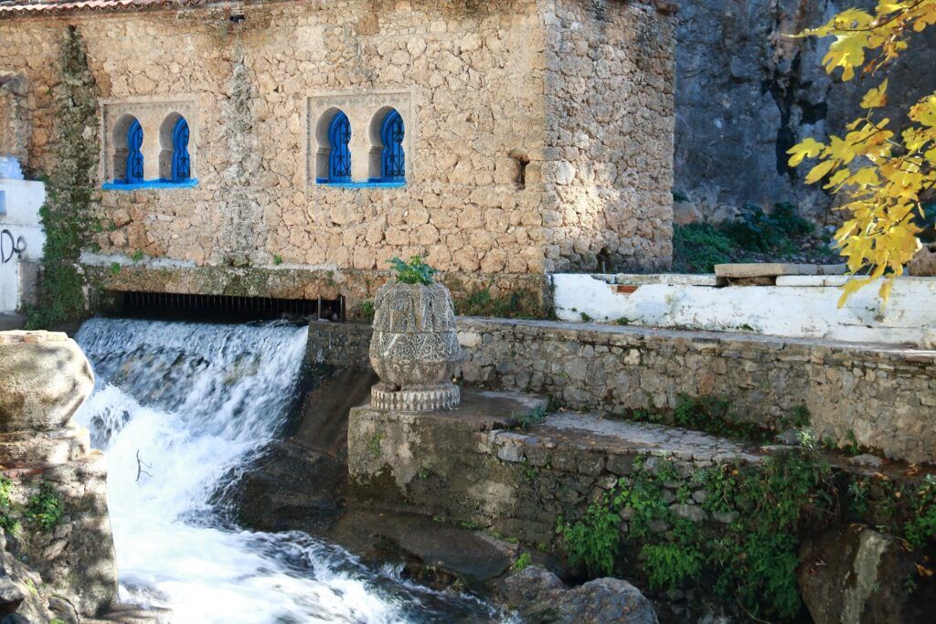Source Ras El Ma, montrant les chutes d'eau et le bâtiment en pierre avec des fenêtres bleues à Chefchaouen.