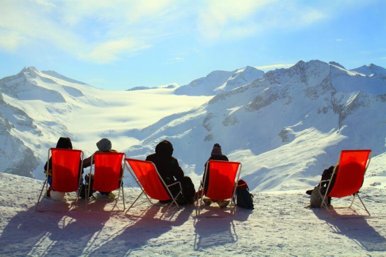 Après-ski : des gens se reposent sur des chaises longues rouges dans la neige, admirant la vallée et les sommets enneigés.