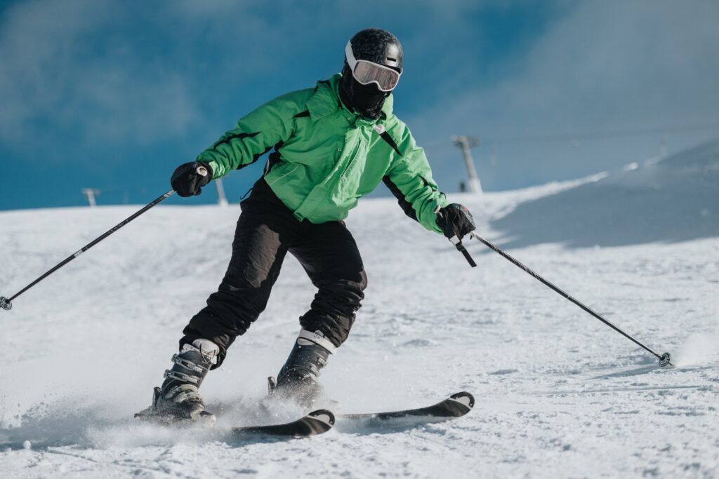 Skieur en veste verte descendant une piste de ski, avec des bâtons.