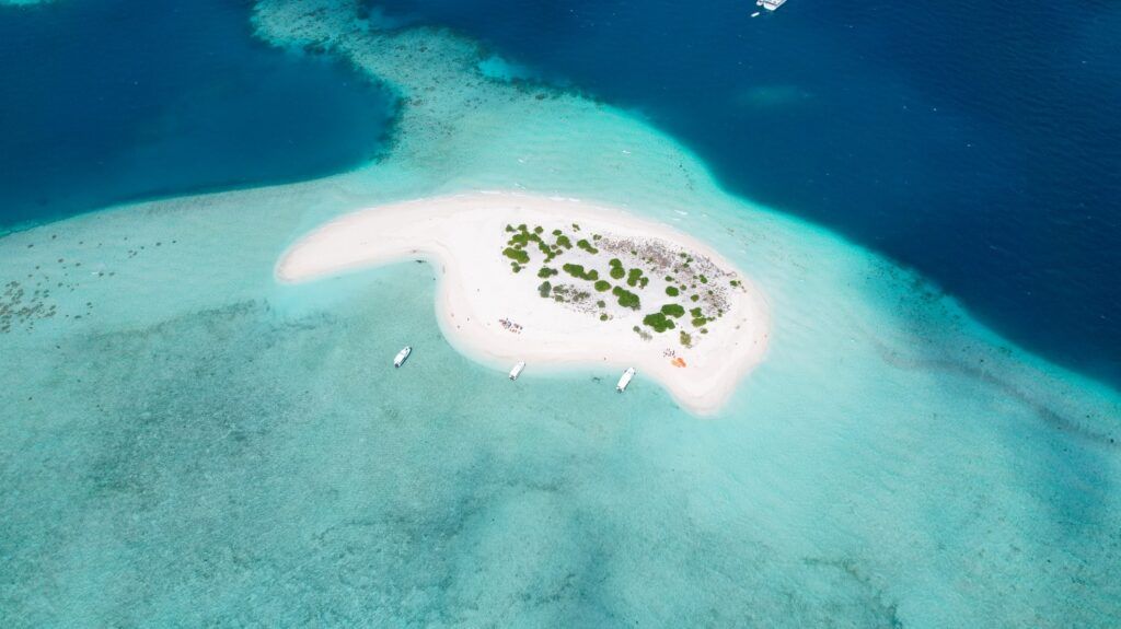 Une vue spectaculaire d'un petit banc de sable blanc aux Maldives, entouré d'une eau turquoise cristalline avec trois bateaux ancrés près du rivage.